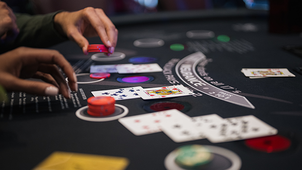 A dealer's hands dealing cards onto a green blackjack table at a casino.