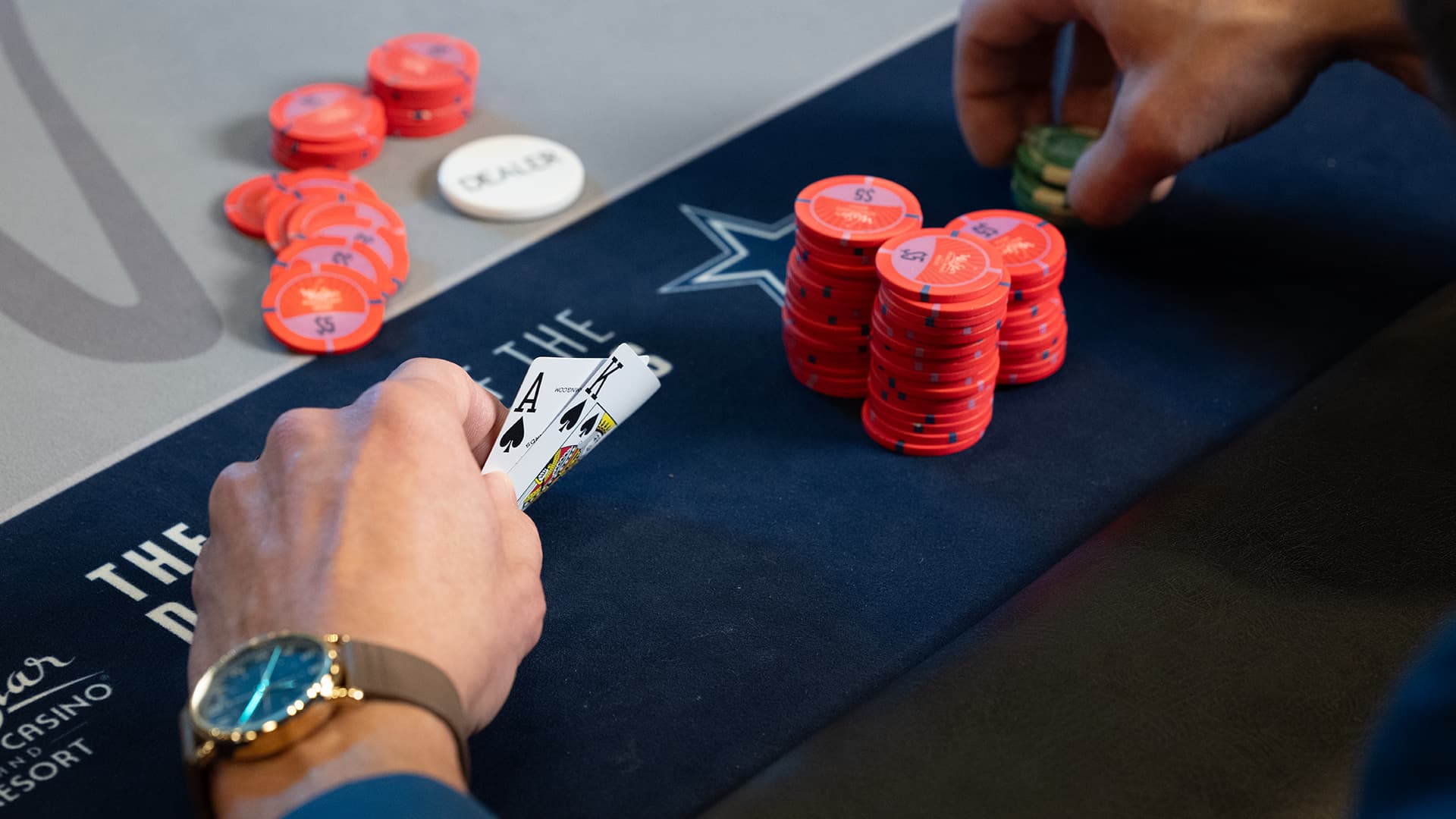 A close-up of a person's hand placing a white poker chip onto a stack of red chips on a poker table.