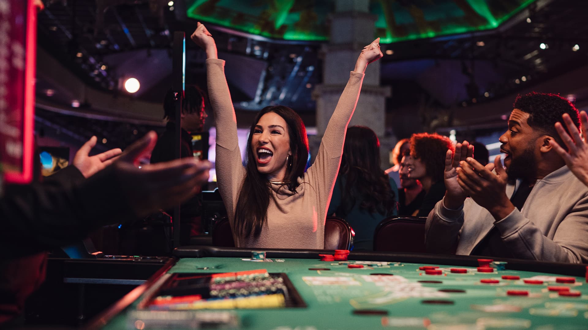 A group of people celebrating and cheering around a Texas Hold'em poker table at a casino.