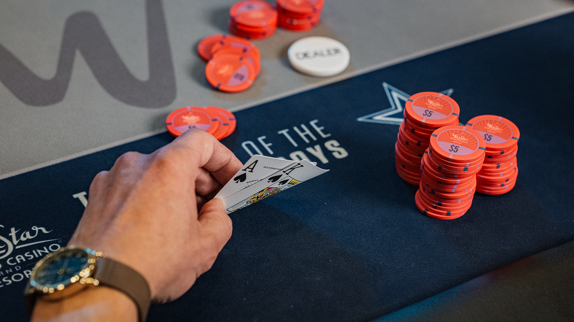 A player’s hands holding two face-down cards next to stacks of poker chips and a dealer button on a green felt table.