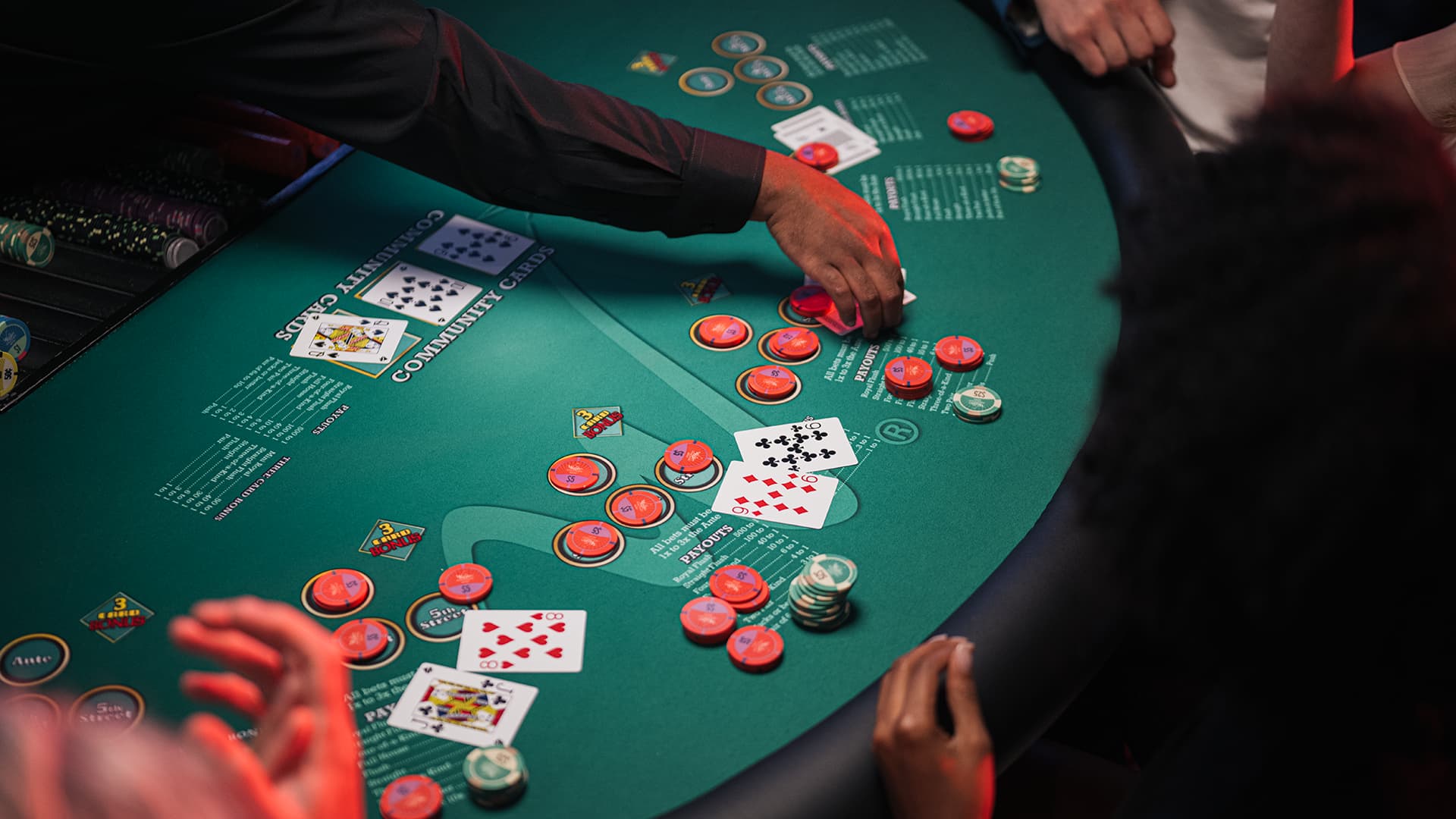A dealer's hands distributing red and white chips across a green felt poker table during a game.