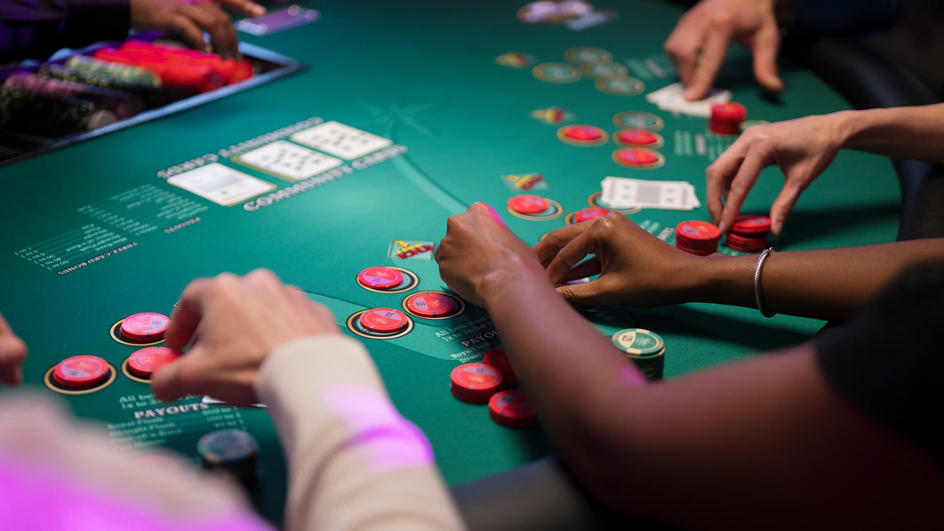 Hands of poker players at a casino table with stacks of betting chips.