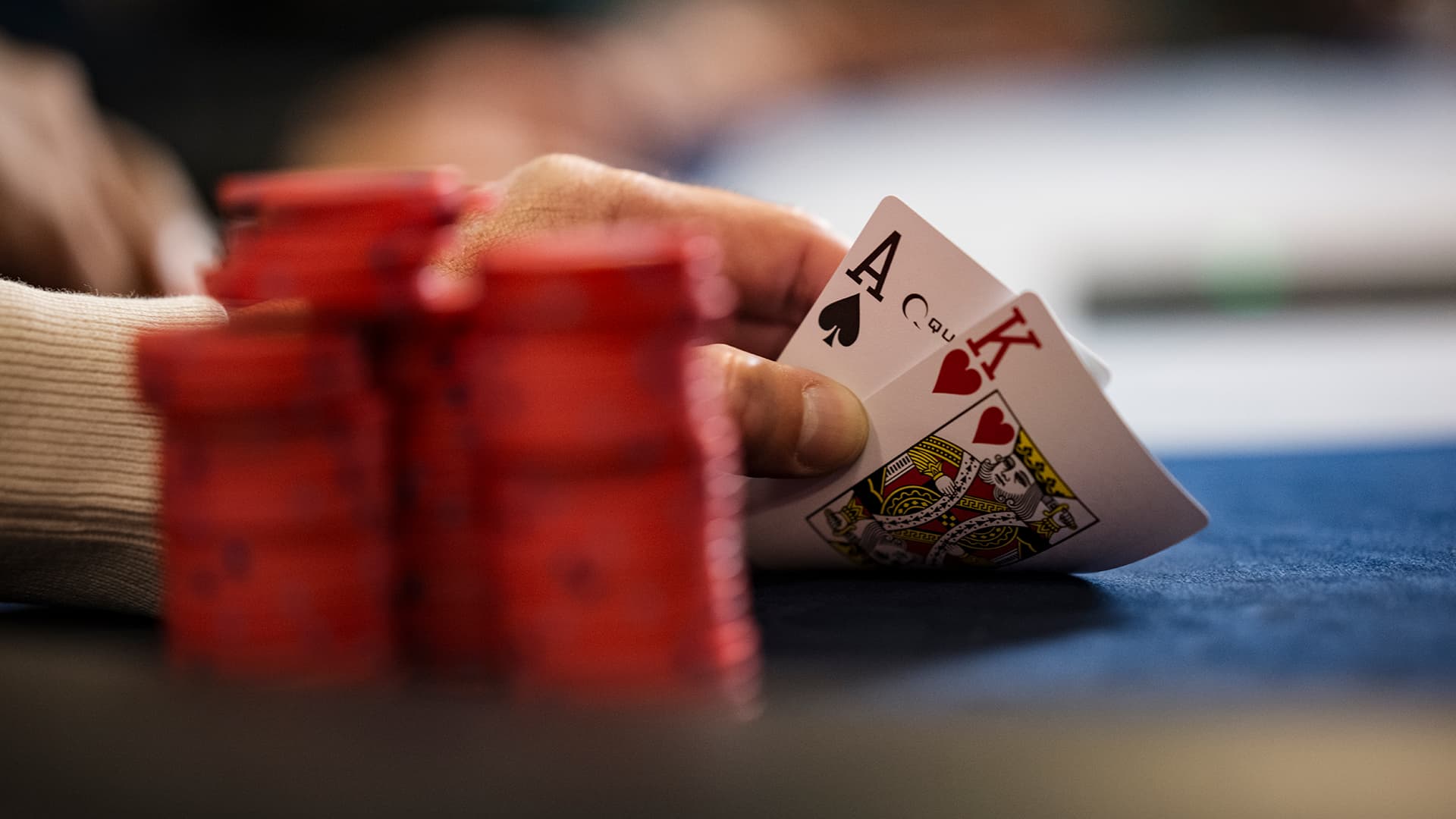 Close-up of a person’s hands holding a winning poker hand of Aces and Kings over a pile of betting chips on a green casino table.