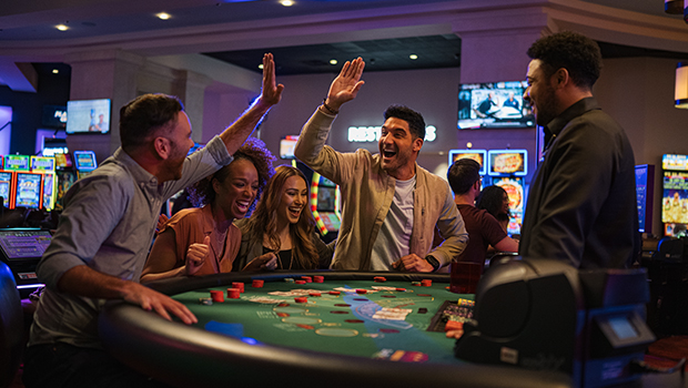 A group of smiling friends celebrating a win at a green-felt blackjack table inside a vibrant, modern casino.