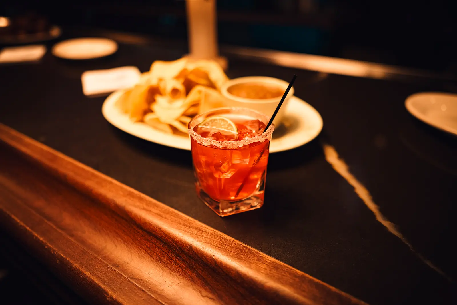 A cocktail on a bar in front of a plate full of food.