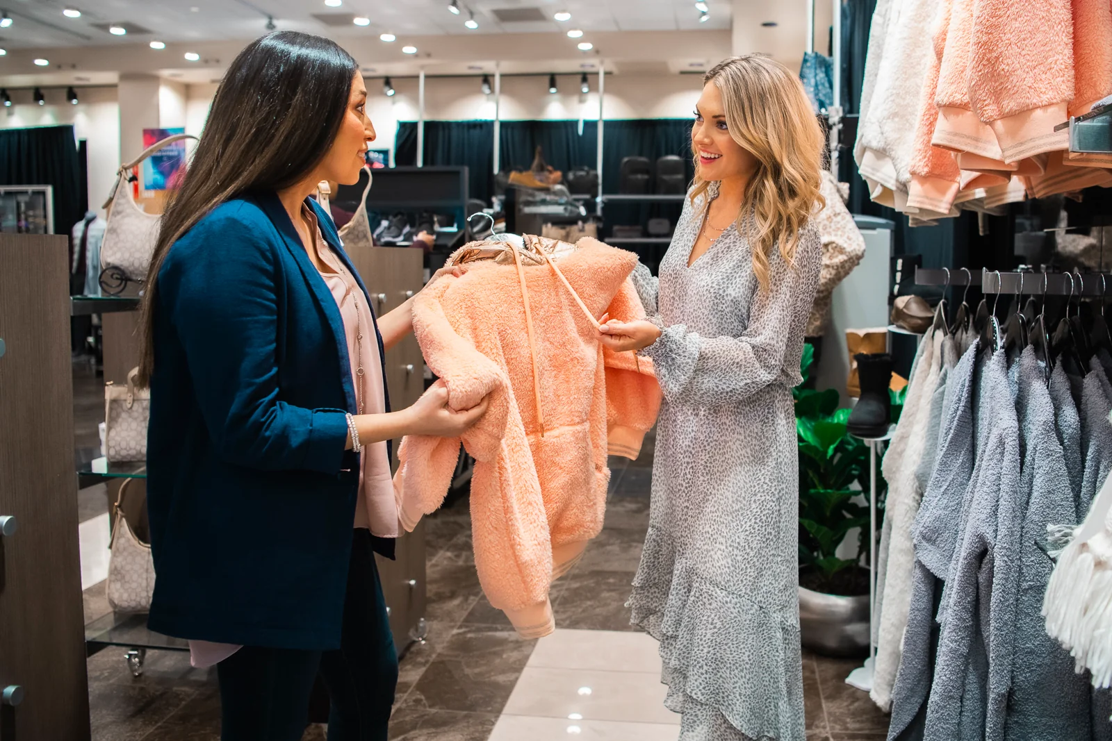 Two women holding a comfy hoodie in Onyx Boutique.