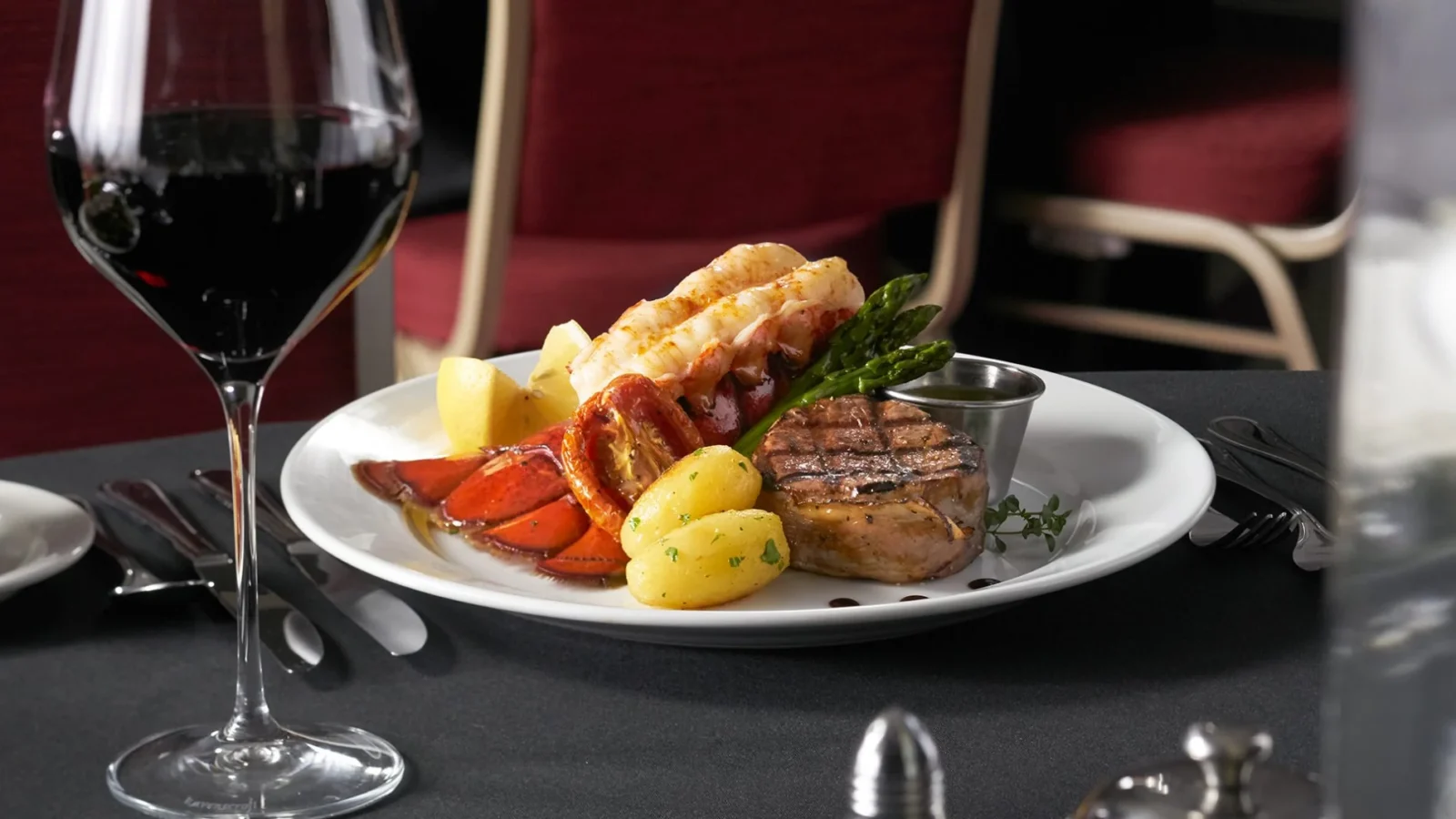 A plate with a surf 'n' turf meal and a large glass of red wine.